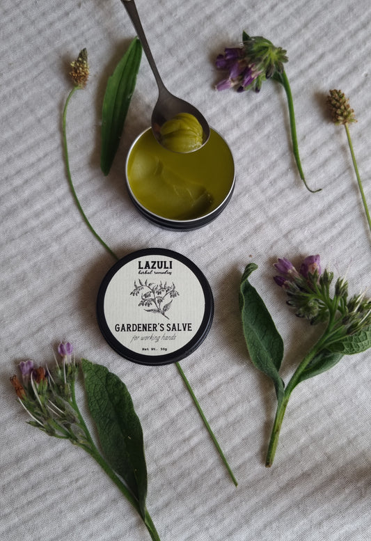 Lazuli Gardener's Salve jar with a spoonful of salve and herbs on a textured surface