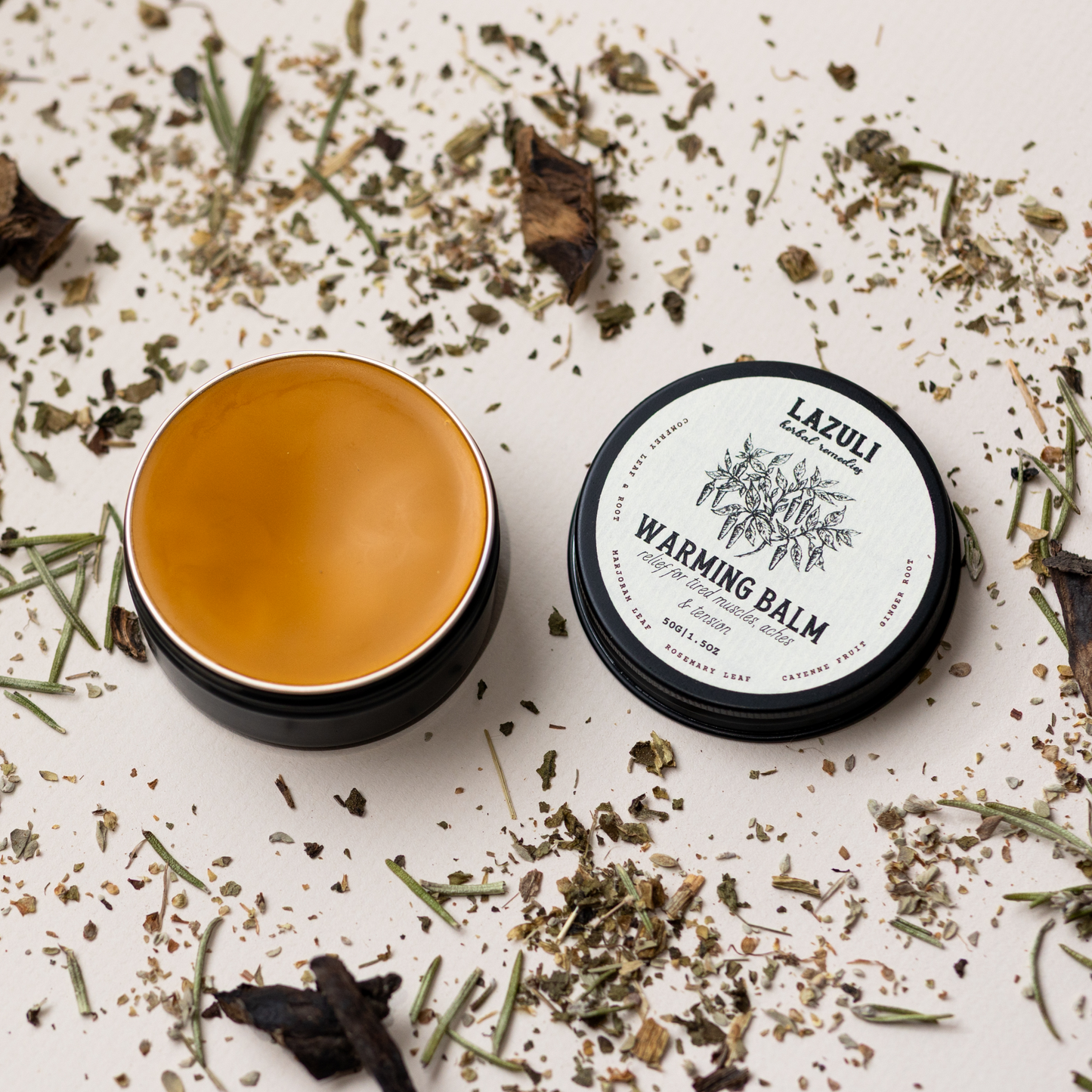 Warming balm container with lid on a white surface with dried herbs